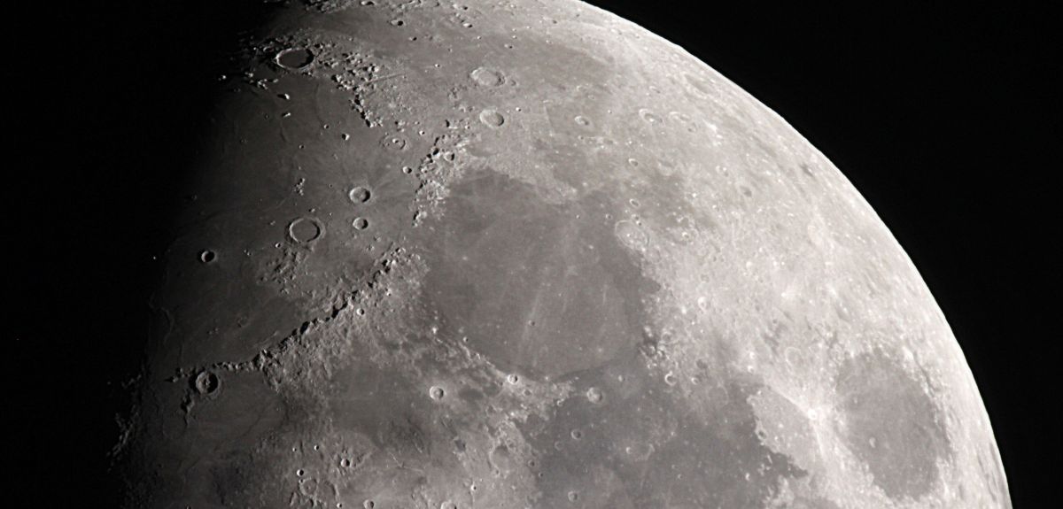 An aerial view over part of the moon, with part of the surface in shadow. 