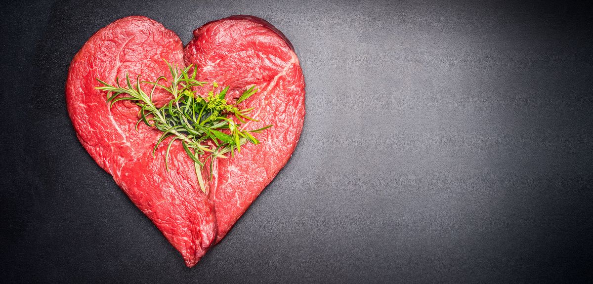 Photo | Heart shape raw meat with herbs on dark chalkboard background