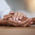 A close up of the hands of a black woman or doctor holding those of a white patient in a hospital setting. Image credit: Shutterstock. 