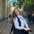 Daphne Harries stands, smiling, in sub fusc in Brasenose Lane