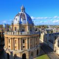 A view looking down over a large dome-shaped building. In the background is an Oxford college; a collection of buildings arranged in four sides around a quadrangle. 