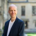 Upper body image of Professor Alexander Betts with blurred picturesque Oxford background