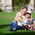 Woman and young girl sit on the grass reading Oxford Open Doors brochure