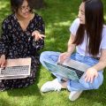 Two people sat on grass with their laptops. 
