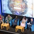 Aerial view of stage with panellists and moderator in discussion with Sheldonian Series graphic on a screen behind them
