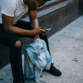 Man sat on wall looking at phone, holding a jacket. Image by Derick Anies on Unsplash. 