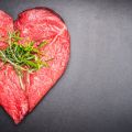 Photo | Heart shape raw meat with herbs on dark chalkboard background